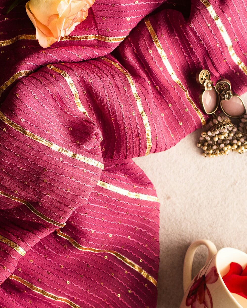 Maroon and gold striped dupatta with jewellery on a cream surface